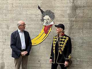 Zwei Personen stehen vor einer grauen Wand, dahinter ein Motiv mit Banane und Beethoven 