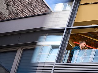 Studierender spielt Saxophon am Fenster in einem Haus. 