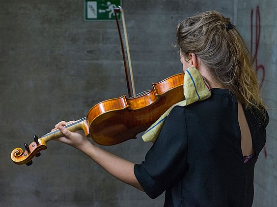 Person steht zum Rücken zur Kamera und spielt auf einer Violine