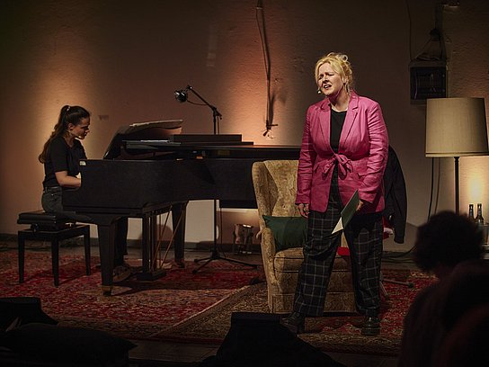 Personen auf der Bühne mit Mikrofon und Klavier