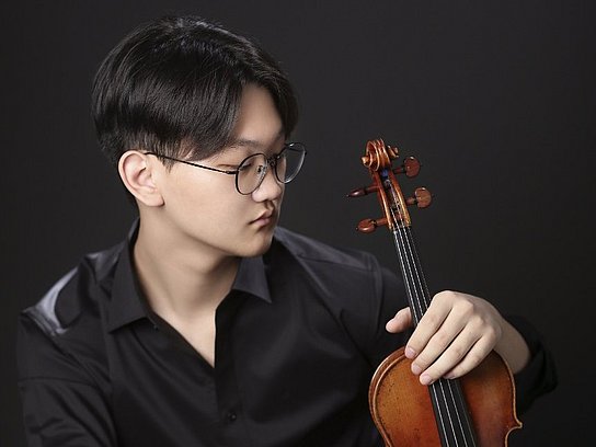 Person hält eine Violine in der rechten Hand und betrachtet sie mit einem konzentrierten Blick. 