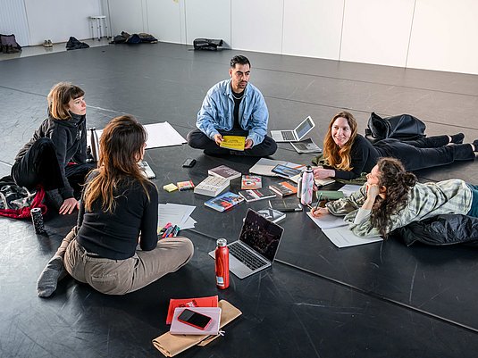 Studierende sitzen auf dem Boden und sprechen miteinander.