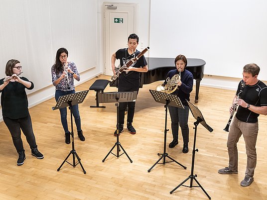 Studierende mit verschiedenen Instrumenten stehen vor Notenpulten und proben