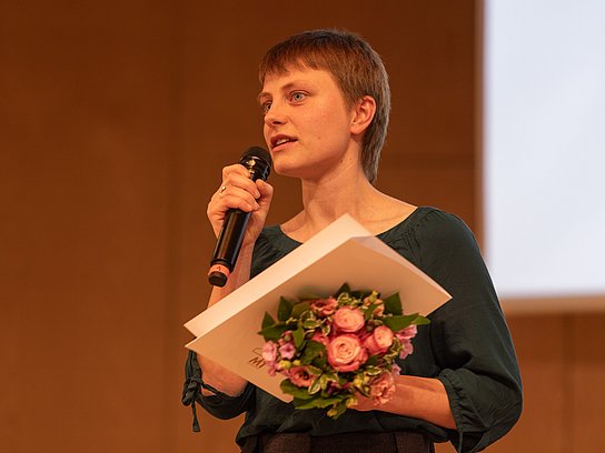 Person mit Mikrofon und einem Blumenstrauß