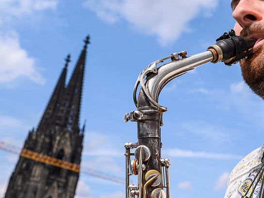 Spitze des Kölner Doms und ein Ausschnitt eines Saxofonspieler*in