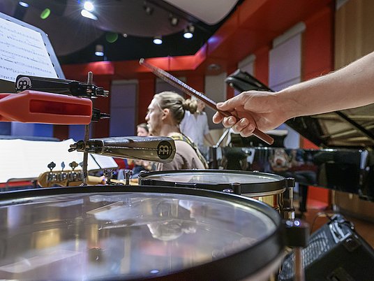 Schlagzeugspieler und Studierender mit Gitarre auf einer Bühne.