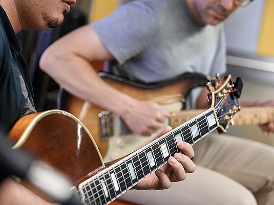 Zwei Personen spielen auf der Gitarre.