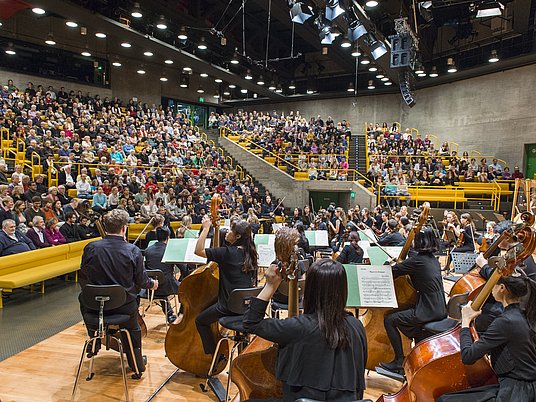 Orchester auf der Bühne mit Publikum im Hintergrund.