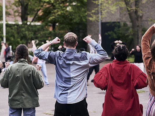 Studierende stehen im Innenhof und studieren eine Choreografie ein.