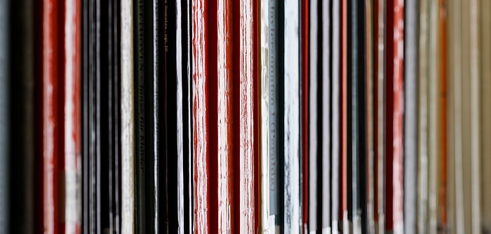 Das Bild zeigt eine Nahaufnahme von dicht aneinander stehenden Schallplattenhüllen in verschiedenen Farben in einem Regal.