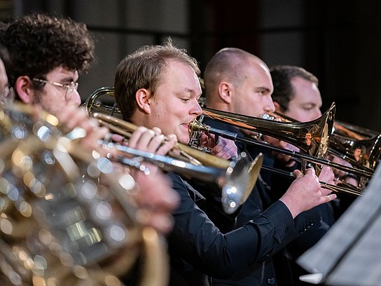 Ausschnitt eines Orchesters mit vier Studierenden und jeweils einem Blasinstrument