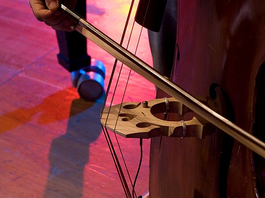 #1601 Es ist der mittlere Bereich eines Kontrabass zu sehen, dessen Saiten von einer hand mit Bogen bespielt werden.