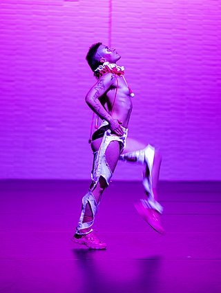 Tanzstudent*in auf der Bühne mit pinker Farbeinspielung.