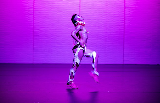 Tanzstudent*in auf der Bühne mit pinker Farbeinspielung.