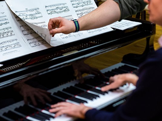 Studierende am Klavier mit Person die Noten umblättert