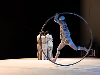 Person steht in einem Ring, dahinter Personengruppe die sich umarmt