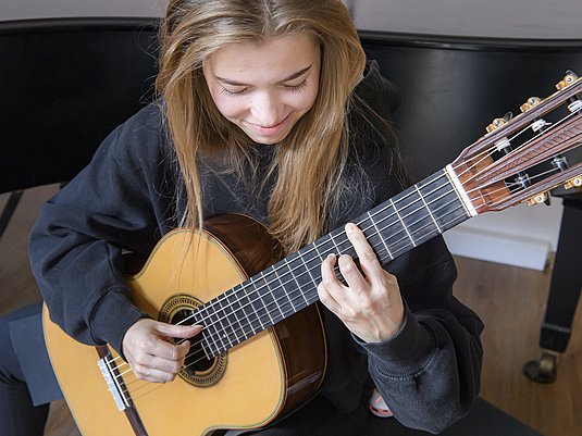 Unterrichtssituation mit einer Studierenden die Gitarre spielt.