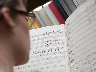 Person schaut sich vor einem Bücherregal Noten an