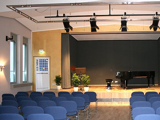 Konzertsaal am Standort Wuppertal mit Stuhlreihen, Blumen und Flügel auf der Bühne.