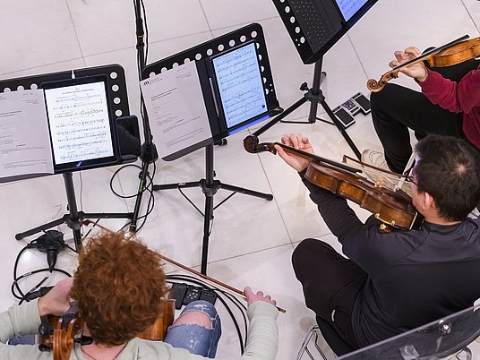 Zwei Studierende spielen Violoncello und Violine von einem Tablet. 