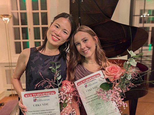 Zwei Personen mit Urkunde und Blumen