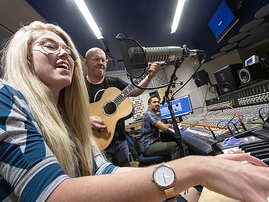 Unterrichtssituation mit einer Studierenden mit Keyboard und Professor mit einer Gitarre im Tonstudio.