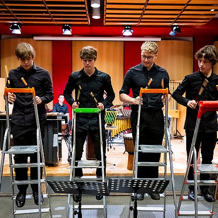 Vier Personen spielen mit Schlagstöcken auf Trittleitern