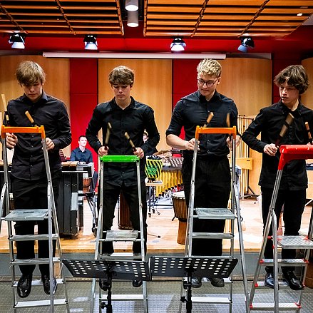 Vier Personen spielen mit Schlagstöcken auf Trittleitern