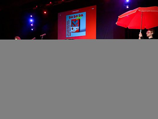 Musizierende Personen auf der Bühne und eine Person hält einen Regenschirm