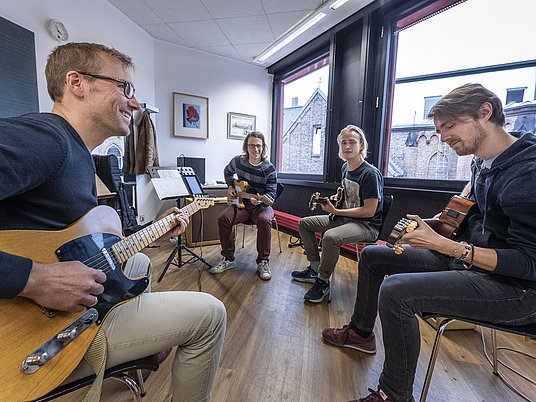 Unterrichtssituation Jazz / Pop mit einem Professor und drei Studierenden mit dem Instrument Gitarre.