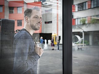 Studierender im Innenhof schaut durch ein Fenster.