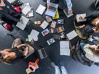 Mehrere Studierende sitzen auf dem Boden und arbeiten gemeinsam